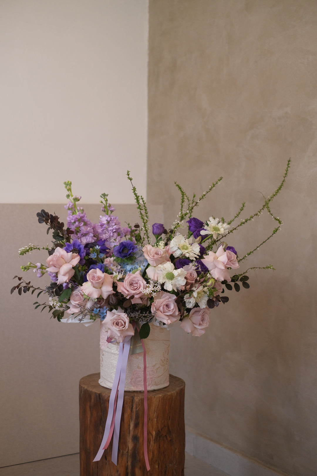 "Floral arrangement with light blue, blush pink, ivory, coral, and pale lavender blooms in embroided box by Bamboo Green Florist"