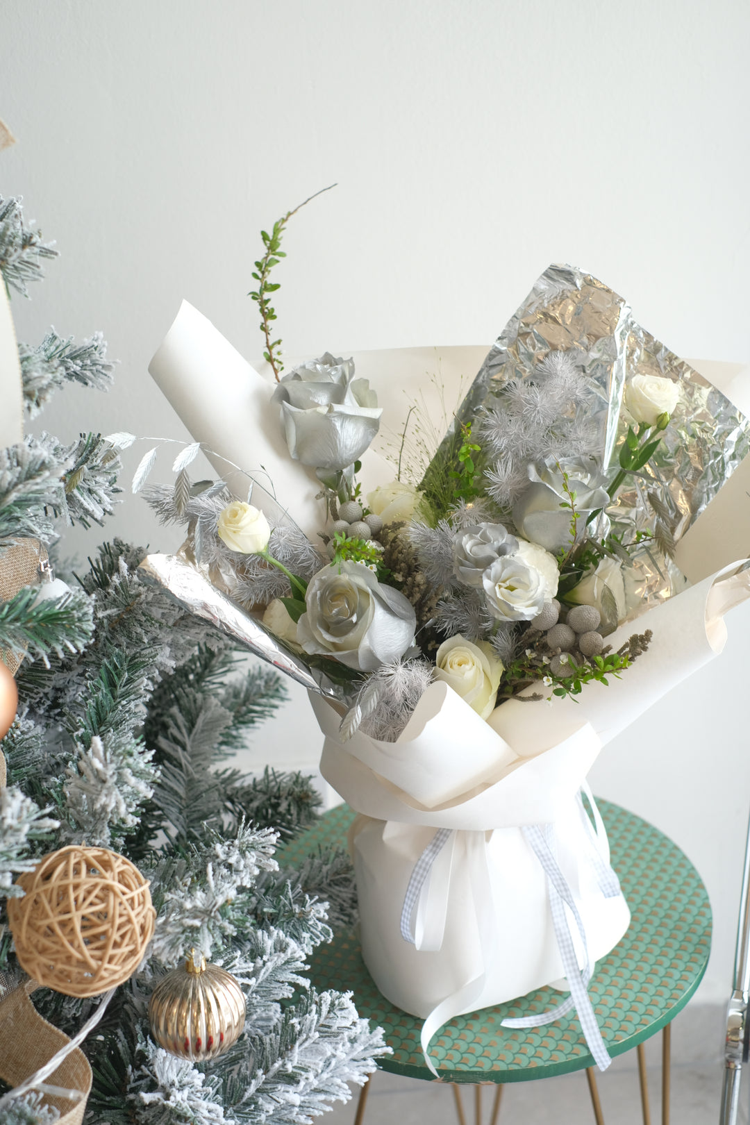 A captivating 'Icy Snow Leigh Fresh Flowers Bouquet' featuring a pristine arrangement of white roses and seasonal Christmas fillers. The delicate white roses resemble freshly fallen snow, and the bouquet is adorned with festive fillers, creating an enchanting winter wonderland vibe. Perfect for holiday tables or as a thoughtful gift, this exquisite bouquet captures the timeless elegance and festive charm of the season."