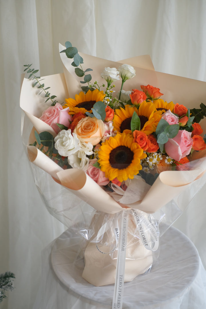 Next Chapter Blooms bouquet by Penang florist Bamboo Green – featuring pink and orange roses with sunflowers, perfect for a sweet lady.