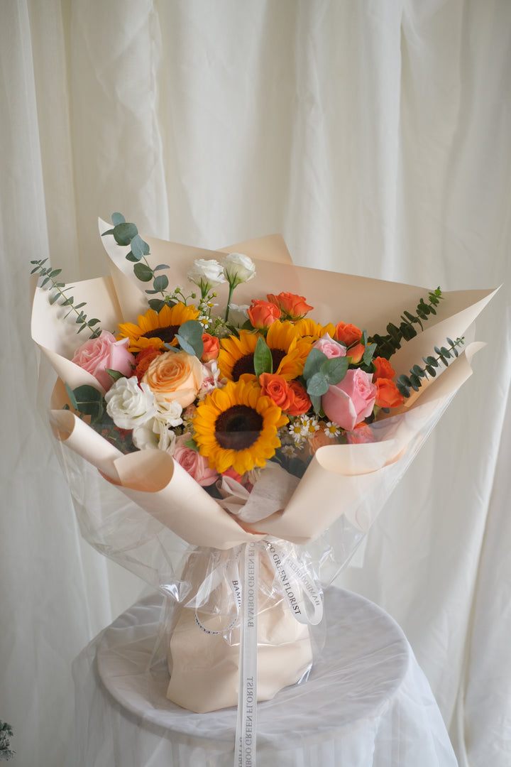 Next Chapter Blooms bouquet by Penang florist Bamboo Green – featuring pink and orange roses with sunflowers, perfect for a sweet lady.