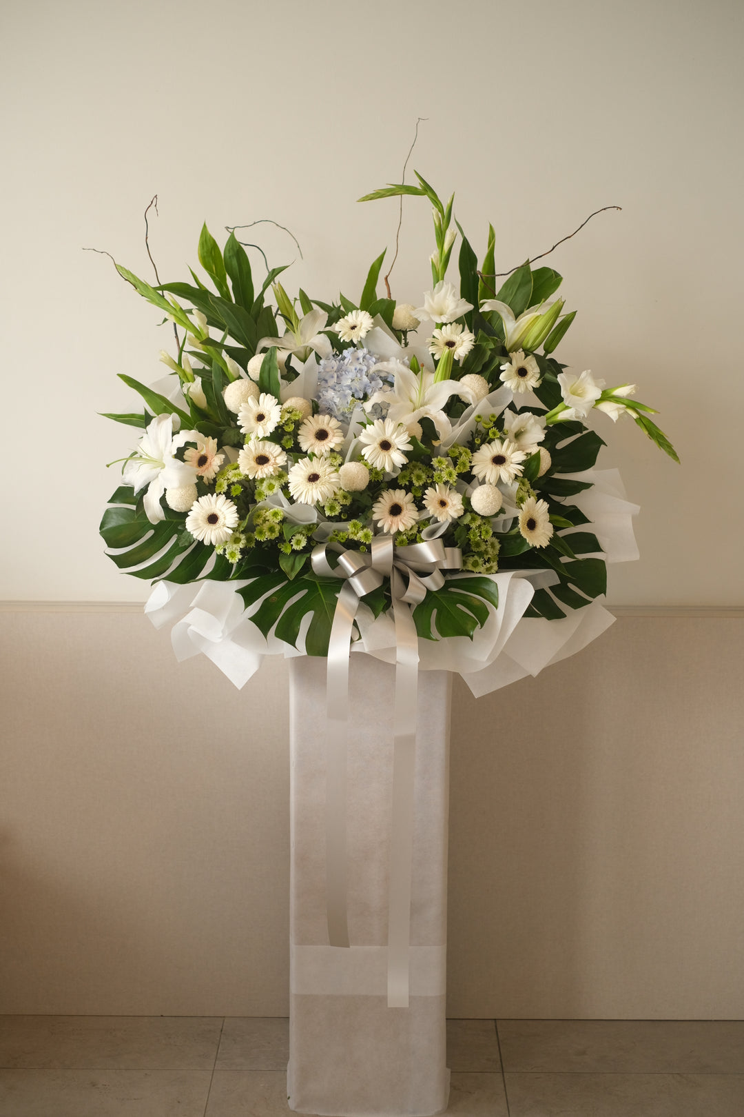 Through this arrangement of white lilies, hydrangeas, and white gerberas, nestled below daisies and greens, we honor and remember the great life of a loved one. This elegant and serene floral tribute from Bamboo Green Florist brings comfort and beauty, a heartfelt gesture to celebrate cherished memories. Available for delivery in Penang