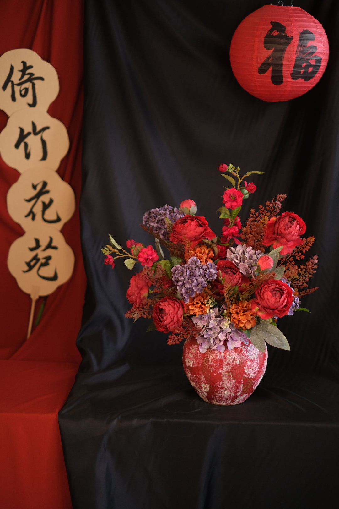 Elegant Chinese New Year floral arrangement featuring vibrant red blooms with purple accents in a red ceramic painted pot, showcasing an oriental design and festive charm.