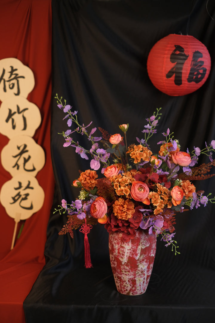 Elegant Chinese New Year floral arrangement featuring vibrant red blooms with purple accents in a red ceramic painted pot, showcasing an oriental design and festive charm.