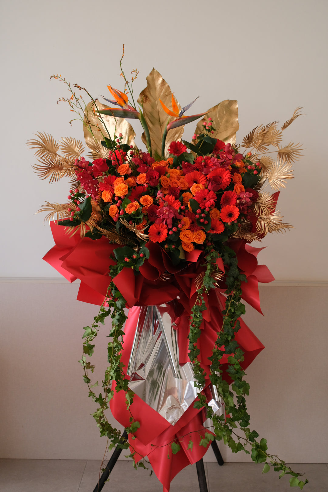 Aurum Rise grand opening flower stand — red and orange blooms with Birds of Paradise, gold leaves, and cascading ivy by Bamboo Green Florist Penang