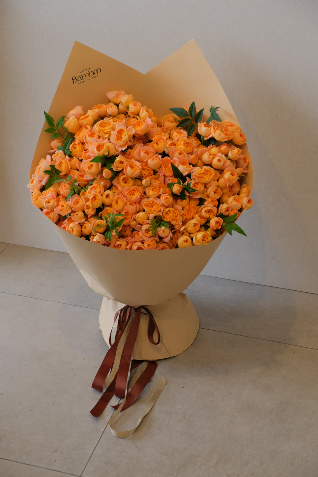 A minimal bouquet of coral-toned multi-head garden roses, paired only with green leaves and wrapped in kraft paper. Natural and luxe in appearance.