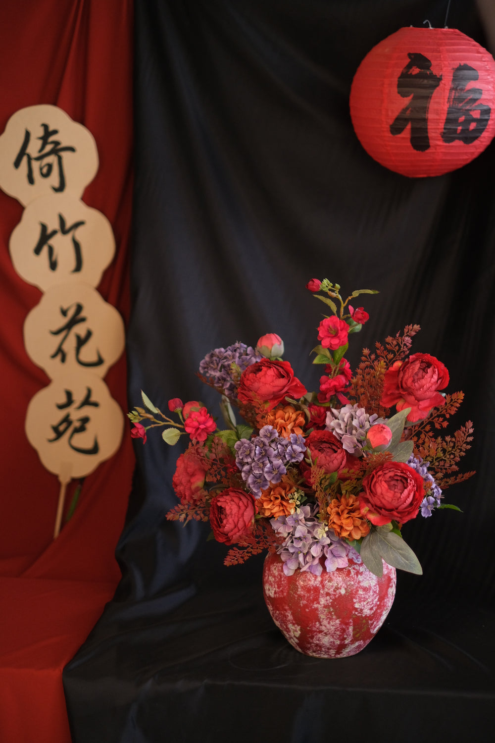 Elegant Chinese New Year floral arrangement featuring vibrant red blooms with purple accents in a red ceramic painted pot, showcasing an oriental design and festive charm.