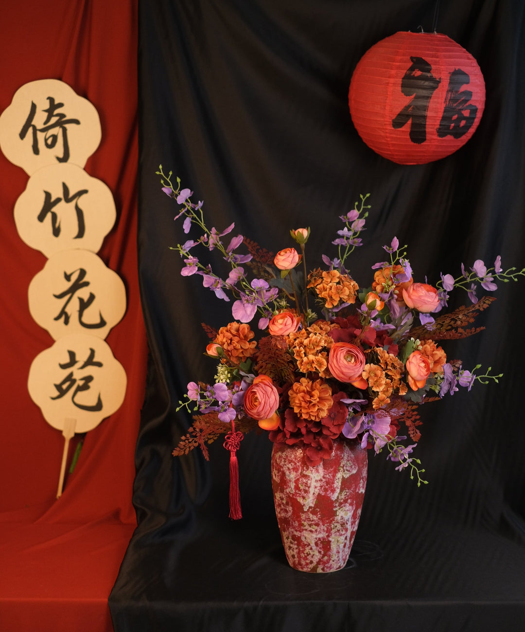 Elegant Chinese New Year floral arrangement featuring vibrant red blooms with purple accents in a red ceramic painted pot, showcasing an oriental design and festive charm.