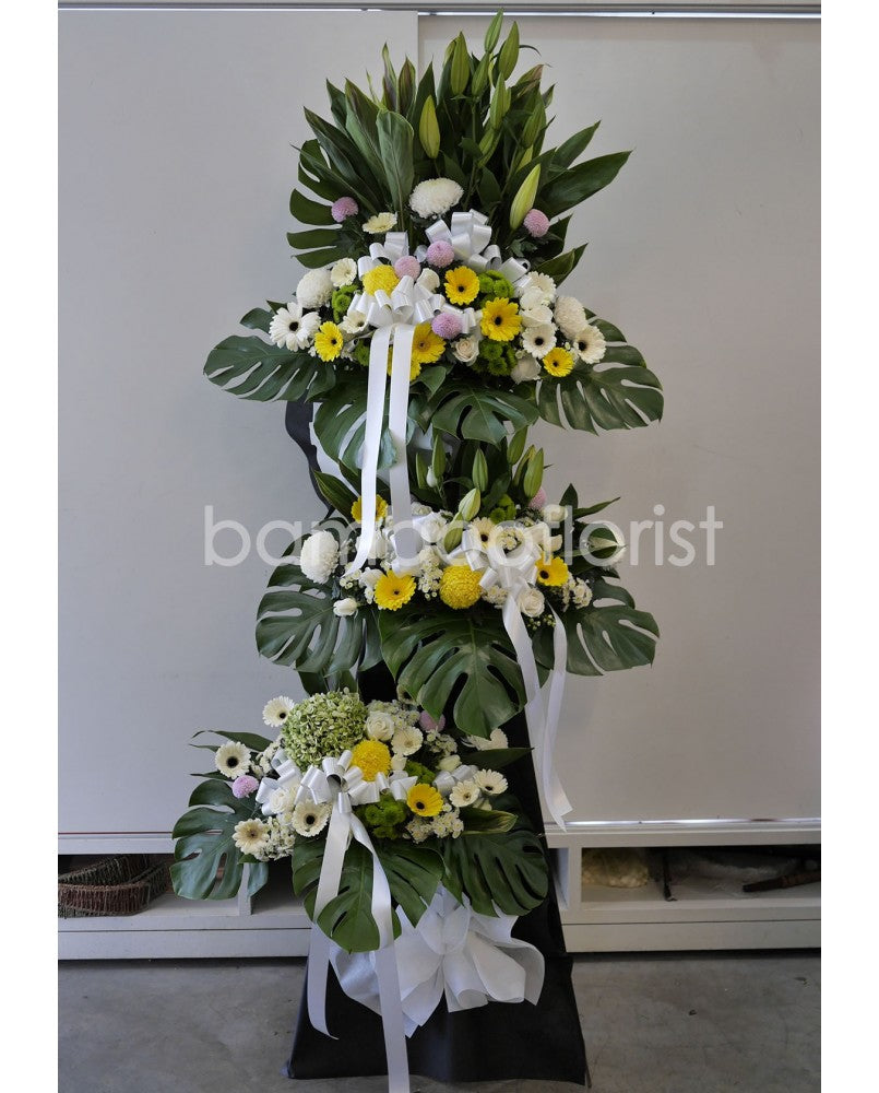 Through this yellow gerbera daisy, poms, white chrysanthemums , burrowed below a backdrop of birds of paradise and greens. A monument in honor of someone dear. For same day condolences flowers delivery in Penang.