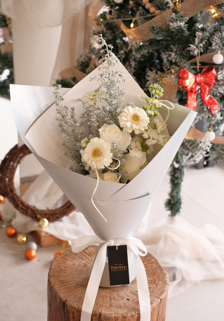 Snowlight bouquet featuring white roses, white gerberas and silvery foliage wrapped in elegant soft grey paper