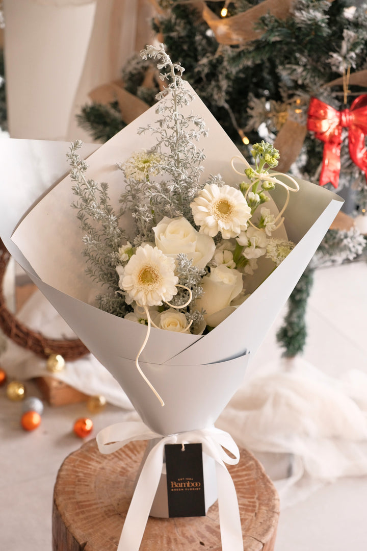 Snowlight bouquet featuring white roses, white gerberas and silvery foliage wrapped in elegant soft grey paper