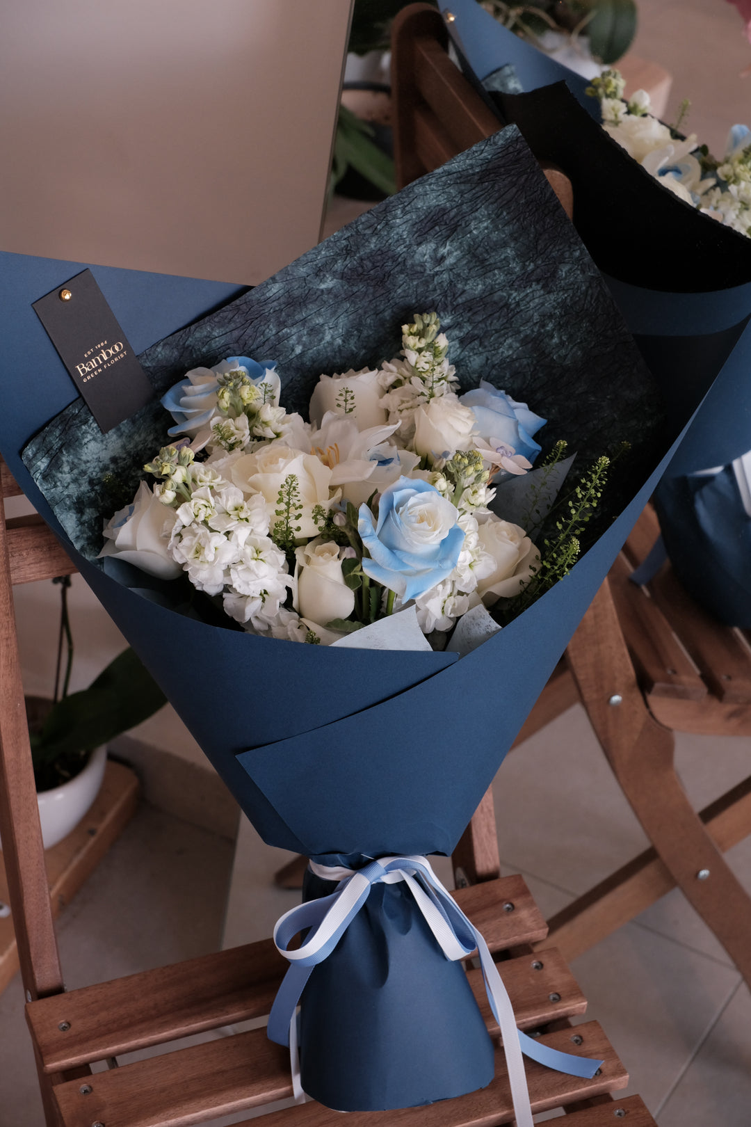 Elegant blue and white omakase bouquet by Bamboo Green Florist Penang, wrapped in signature deep blue sculpted wrap, featuring roses and delphiniums.