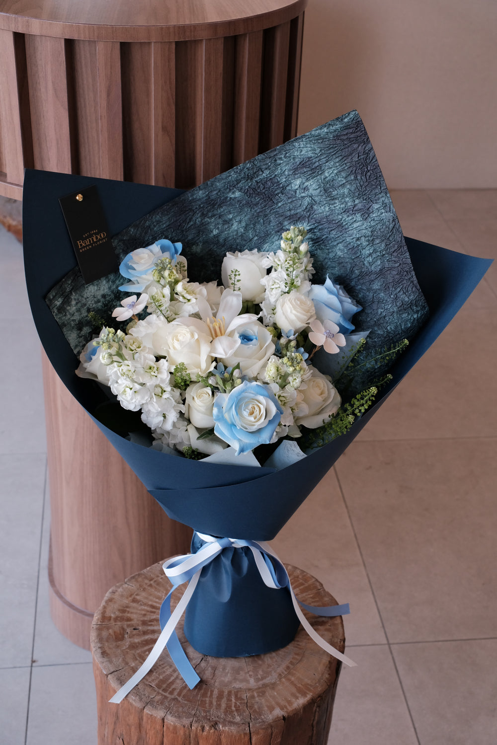 Elegant blue and white omakase bouquet by Bamboo Green Florist Penang, wrapped in signature deep blue sculpted wrap, featuring roses and delphiniums.