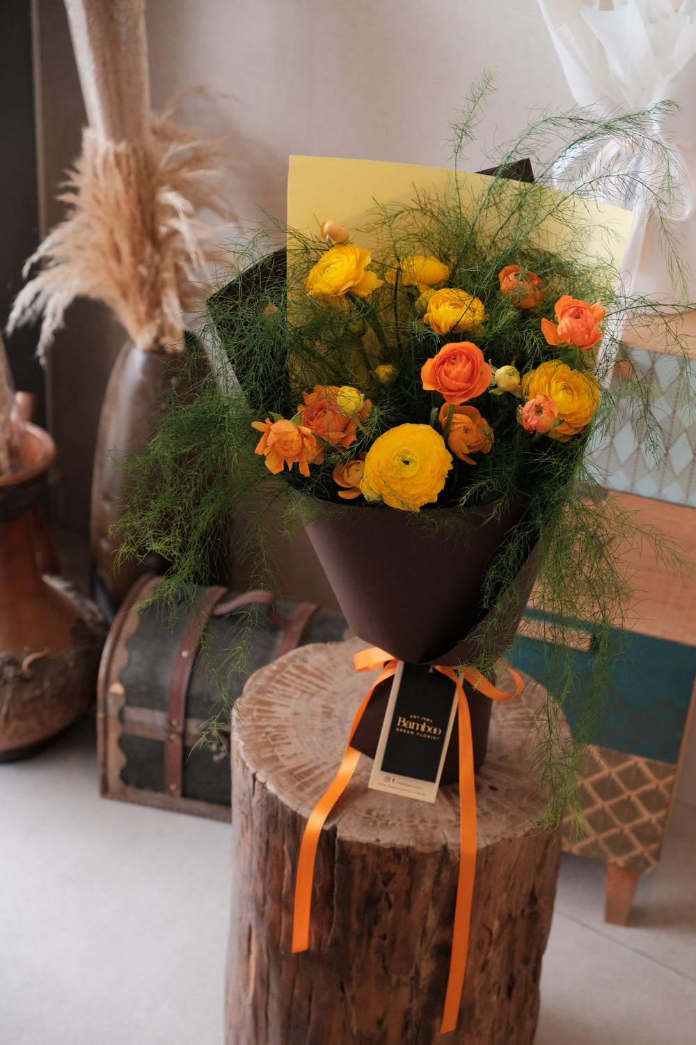 Close-up of pastel ranunculus bouquet wrapped in dark brown paper with flowy grass accents