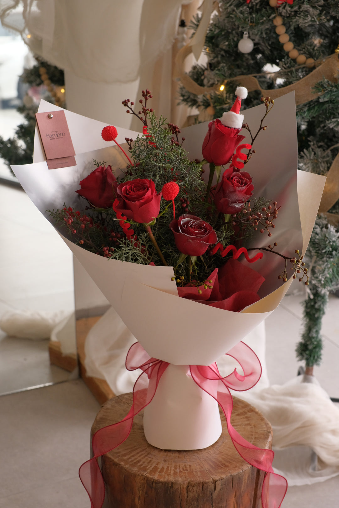 Christmas Eve Rose bouquet with red roses, festive evergreen foliage and Christmas accents, wrapped elegantly for holiday gifting