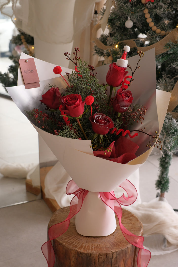 Christmas Eve Rose bouquet with red roses, festive evergreen foliage and Christmas accents, wrapped elegantly for holiday gifting