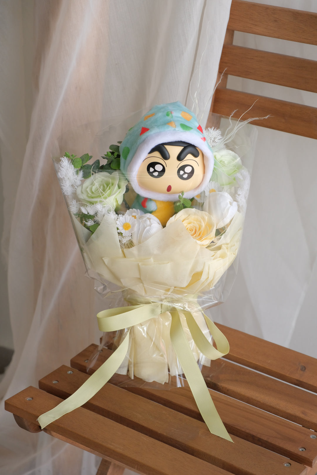 A plush Crayon Shin-chan hugging a pastel red and pink flower bouquet, styled playfully for gifting.

