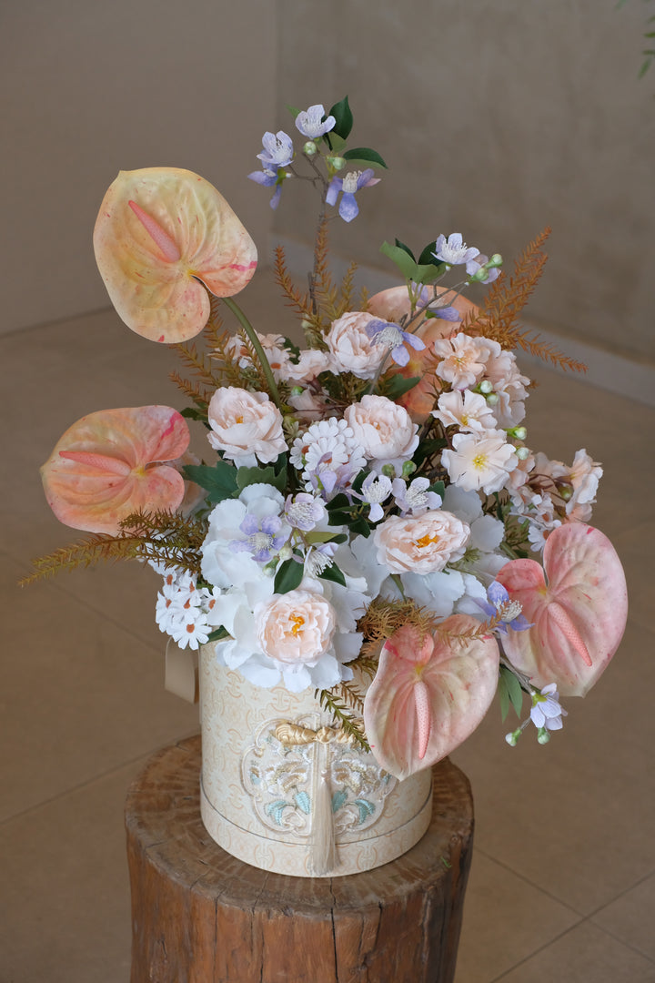 Artificial floral arrangement with peach anthuriums and soft blue accents