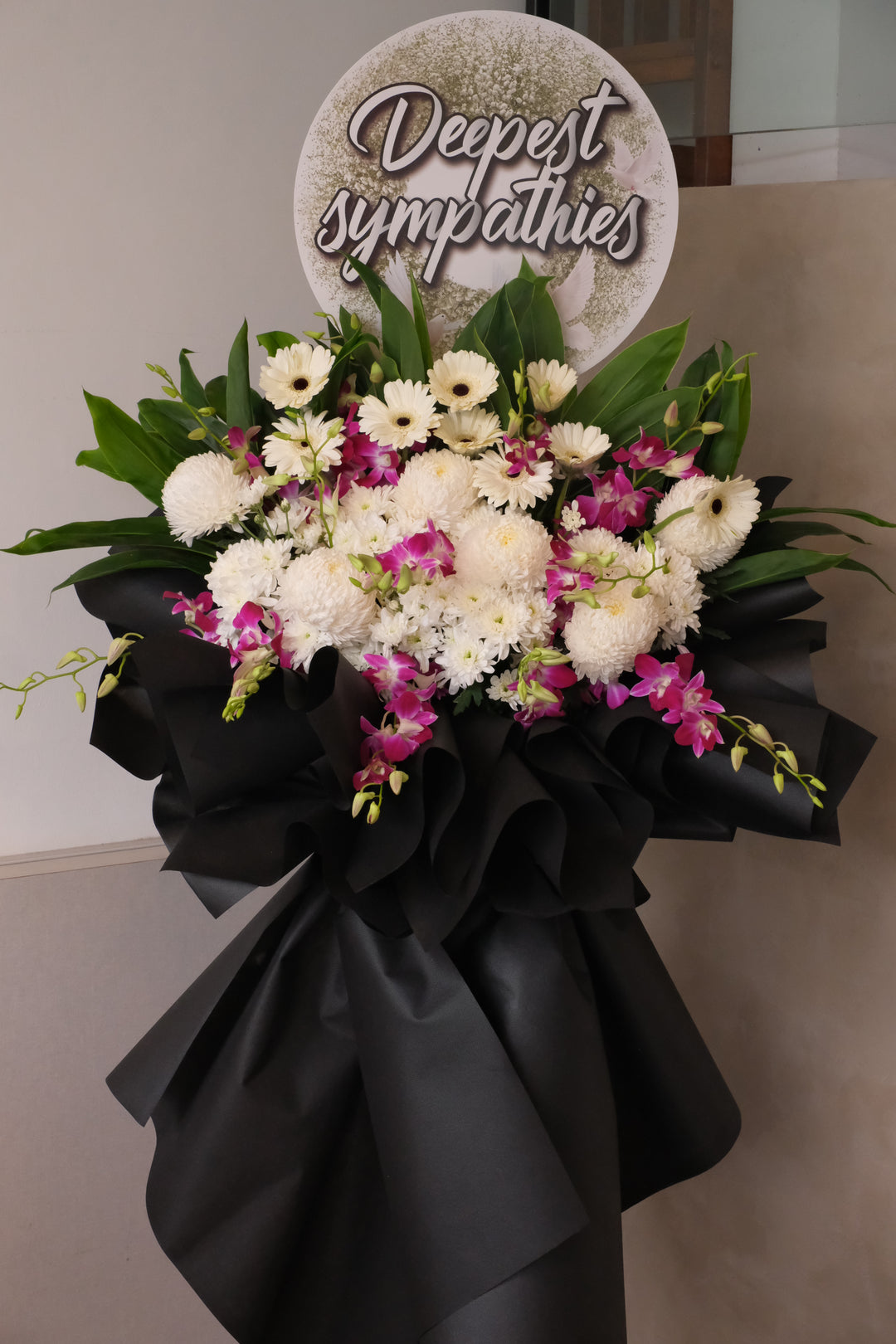 Condolence flower arrangement with white gerberas, pompoms, and purple Sonia orchids, designed with lush greens