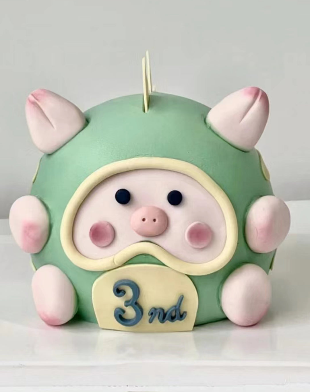 An adorable, customized Lulu Pig fondant cake made in Penang, featuring a pink piglet with big eyes, a sweet smile, tiny ears, and a curly tail. The pig sits on a grassy fondant base, bringing a playful, farm-themed vibe. The cake has multiple layers inside, making it both delightful and delicious—perfect for special celebrations in Penang