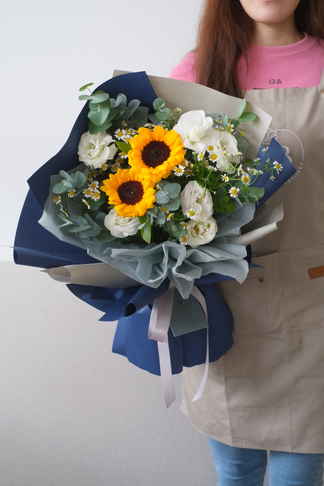 An arrangement that radiates pure happiness! Perfect for birthdays, expressing gratitude, or simply brightening someone's day. This bouquet features cheerful sunflowers, elegant white eustoma, charming chamomiles, and fragrant eucalyptus, all beautifully arranged in a navy and grey wrap