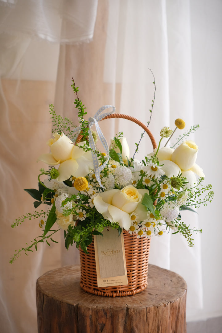 A petite woven basket featuring yellow buttercup roses and mini seasonal blooms. Bright, cheerful, and perfect for uplifting someone’s day or styling a cosy space.