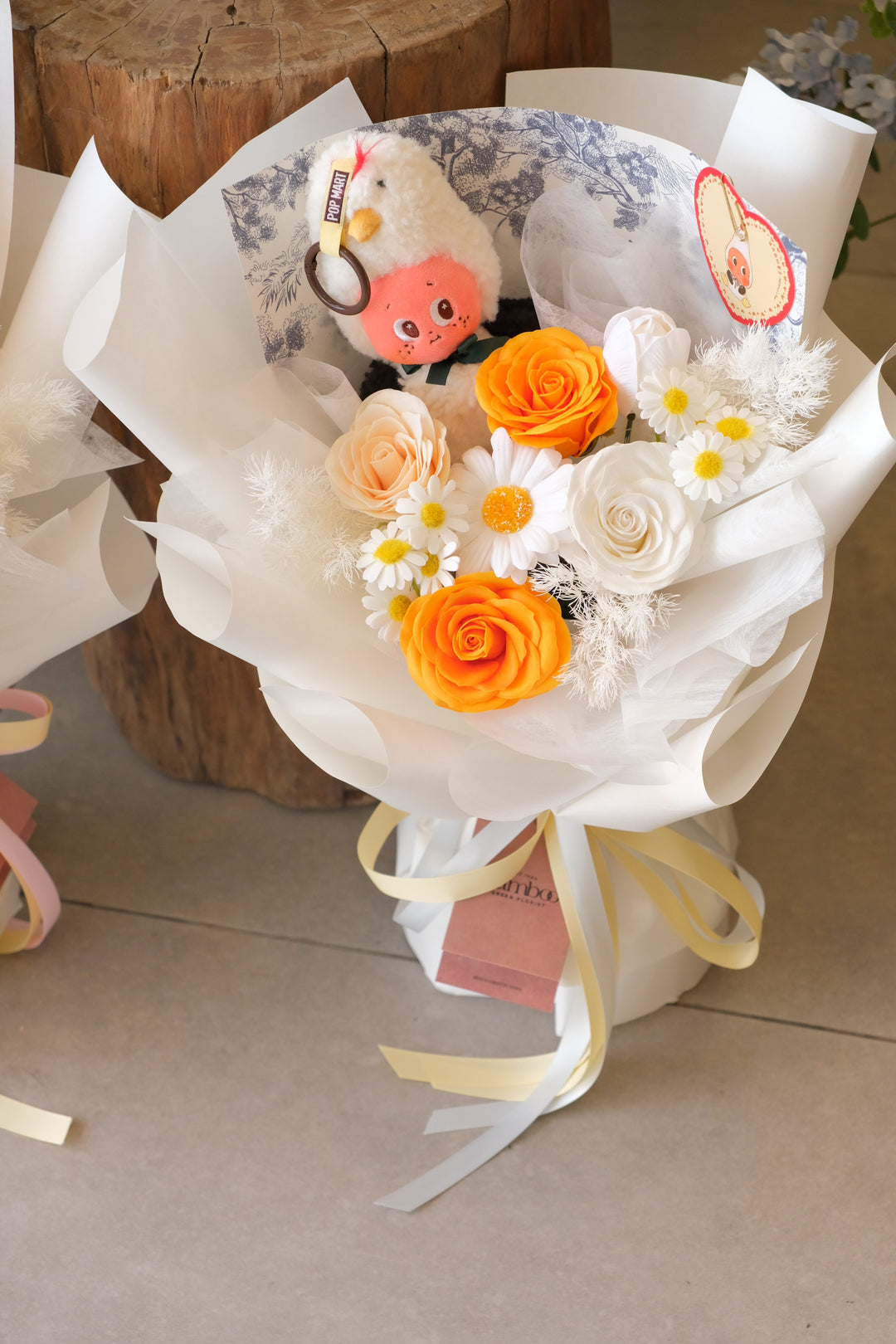 Pop Mart Albatross's Vow character in a soap flower bouquet with orange and white roses, modern white gift wrap by Bamboo Green Florist.