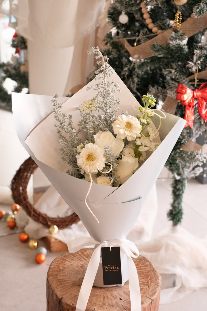 Snowlight bouquet featuring white roses, white gerberas and silvery foliage wrapped in elegant soft grey paper.