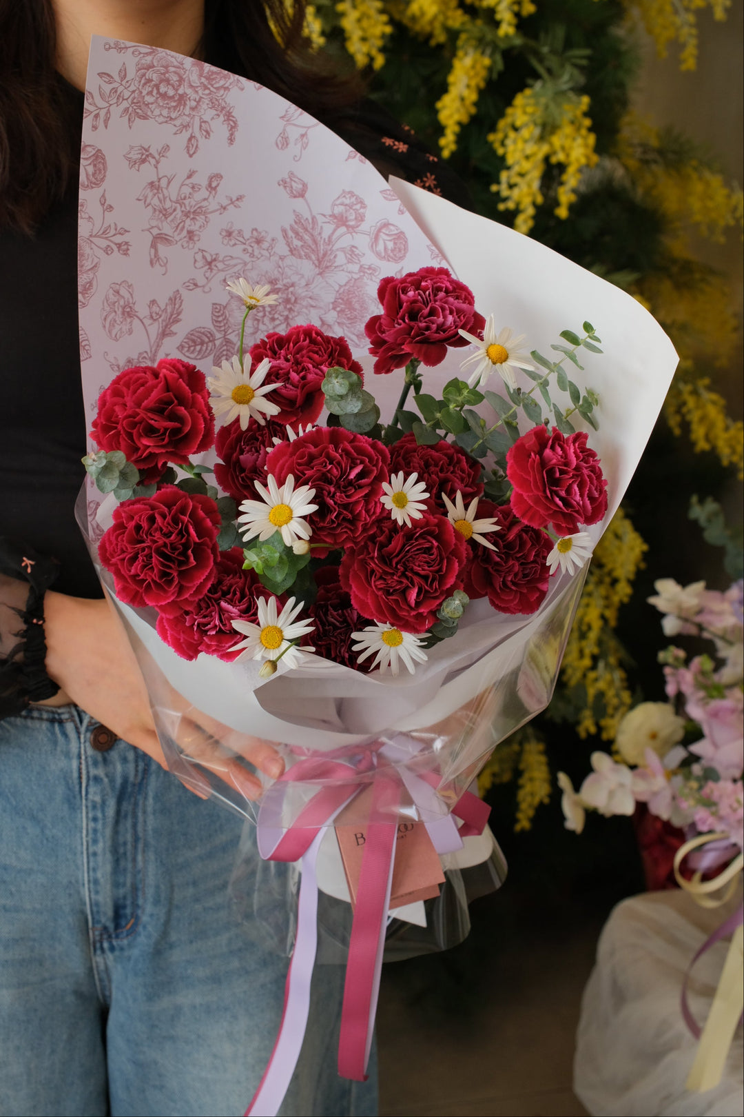 deep red carnations in a bouquet with red wraps.