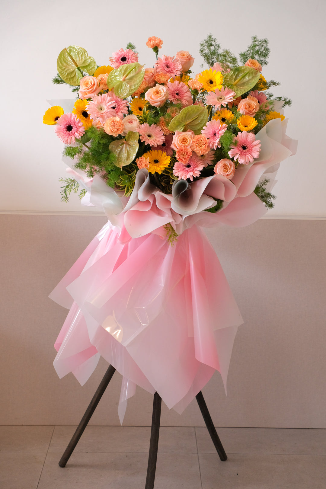 Abundant grand opening floral stand with peach roses, pink and yellow gerberas, and green anthuriums in pink decorative wrapping.