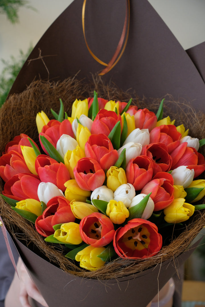 Bouquet of red, yellow, and white tulips in a brown paper wrap.