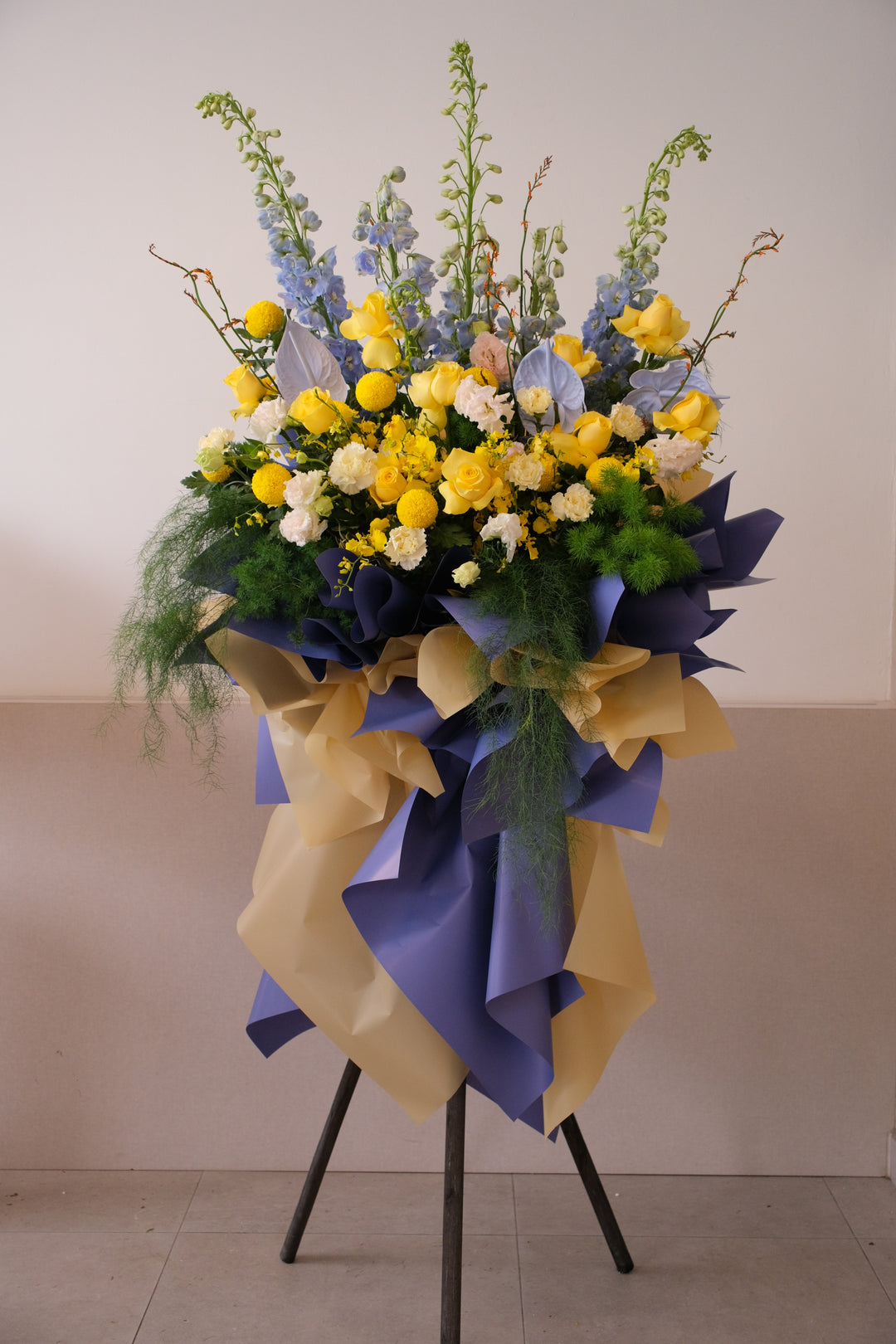Luxury grand opening floral stand with blue delphinium and yellow roses, modern tripod flower arrangement for corporate events.