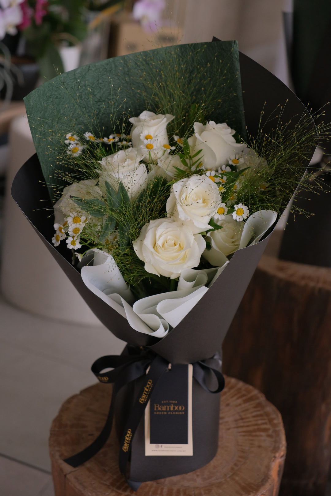 Luxury bouquet of white roses with green foliage wrapped in dark green and black paper