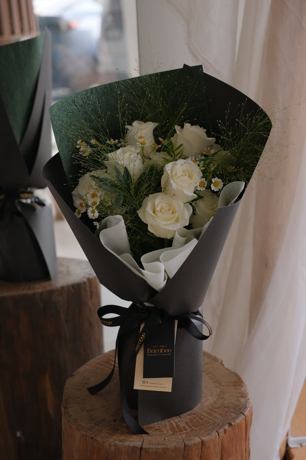 Luxury bouquet of white roses with green foliage wrapped in dark green and black paper