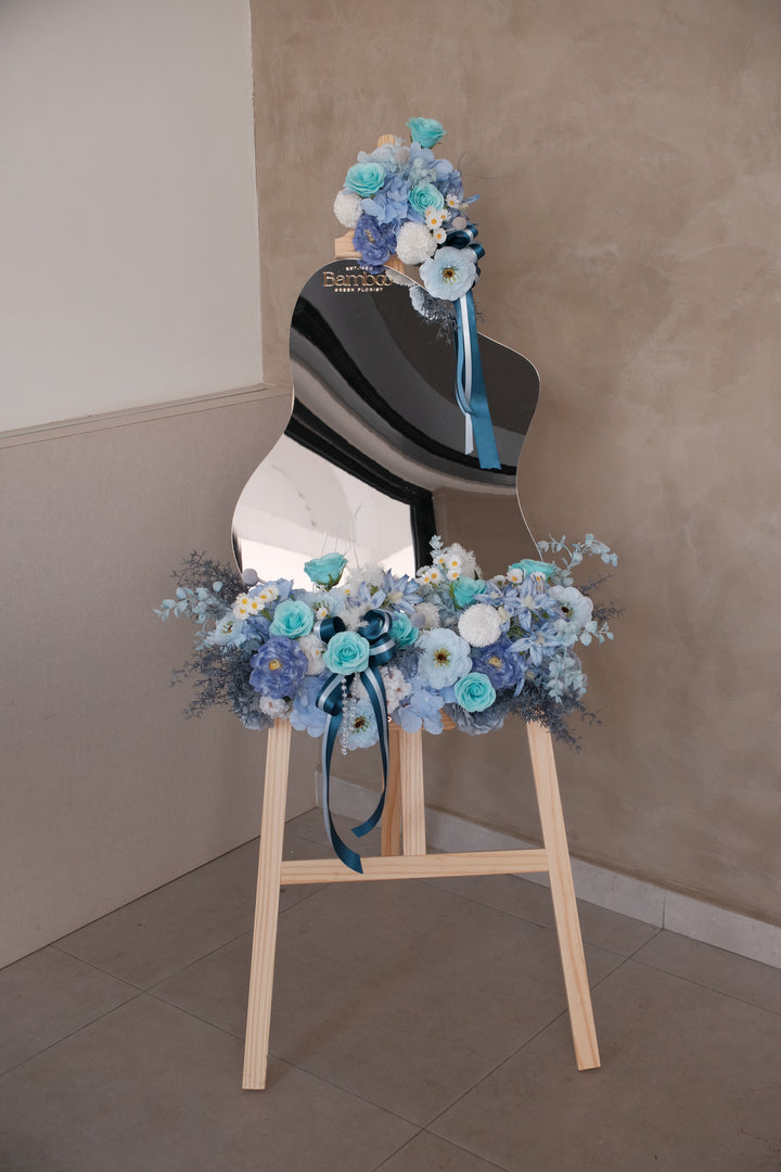 Ophelia Acrylic Mirror featuring a handcrafted blue-themed artificial floral arrangement with elegant ribbons, customizable message panel, and wooden display rack. Perfect for events, gifting, and tabletop decoration.
