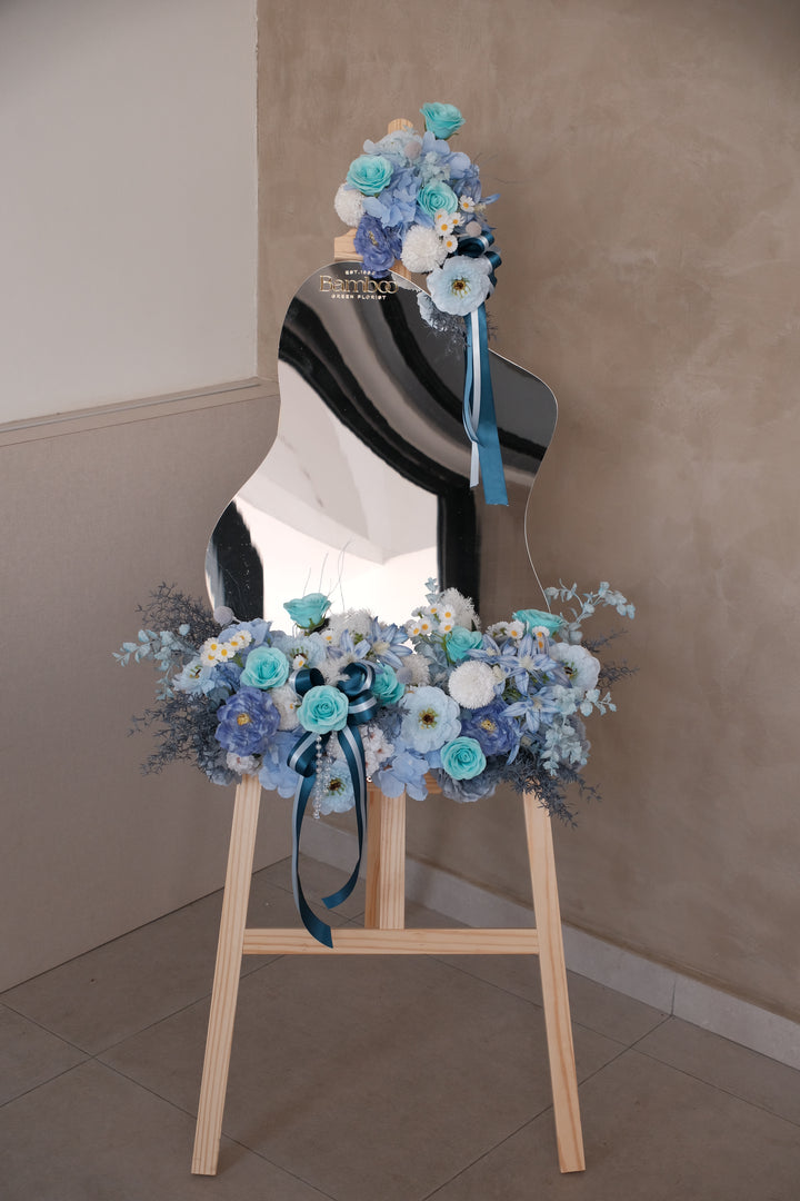 Ophelia Acrylic Mirror featuring a handcrafted blue-themed artificial floral arrangement with elegant ribbons, customizable message panel, and wooden display rack. Perfect for events, gifting, and tabletop decoration.