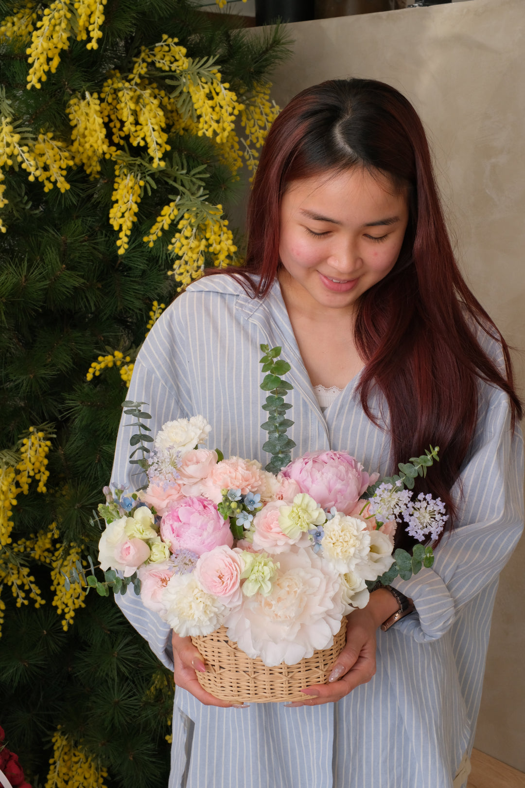 Woman holding a bouquet of fresh peonies  with a basket, surrounded by greenery

