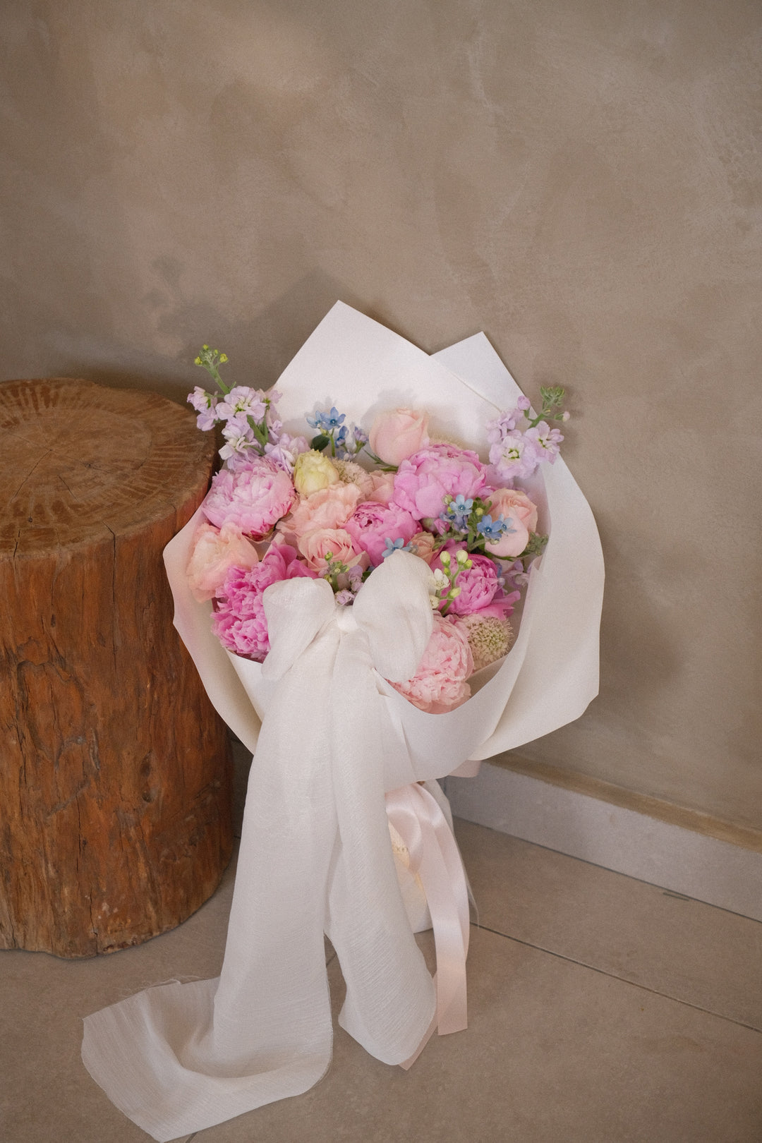 Minimalist bouquet of pink peonies and mixed roses wrapped in white hard wrap with sheer white ribbon.
