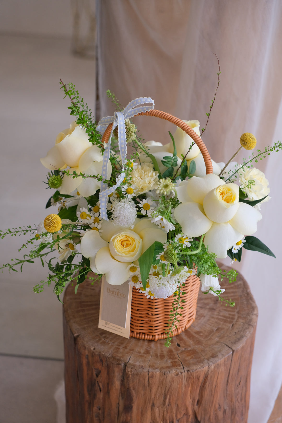 Small woven basket with yellow buttercup roses and mini seasonal flowers arranged in a bright, cheerful style.