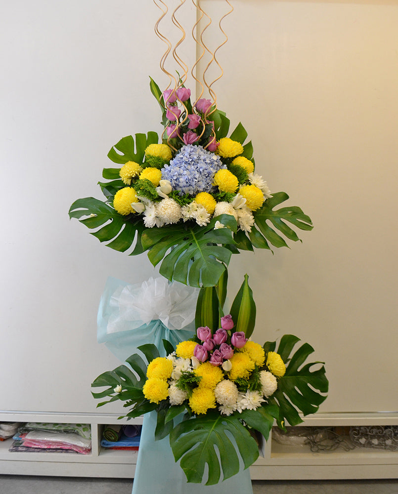 2 tier arrangement featuring yellow and white chrysanthemum, purple roses, blue hydrangea and white poms. For same day condolences flowers delivery in Penang.