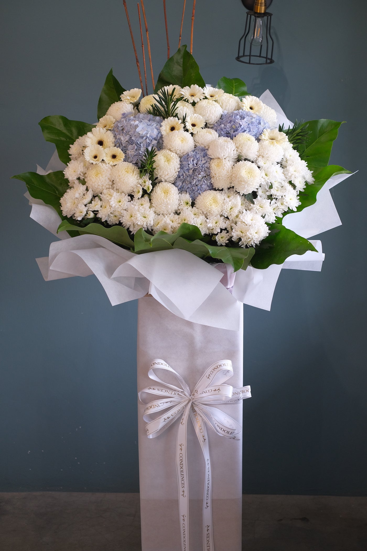 Condolences Flowers delivery to Penang. This beautiful, bright white flowers and soothing blues create a peaceful presentation at any funeral or wake. The classic condolences wreath is delivered on a two tier stand, and is a gracious expression of sympathy and appreciation. 