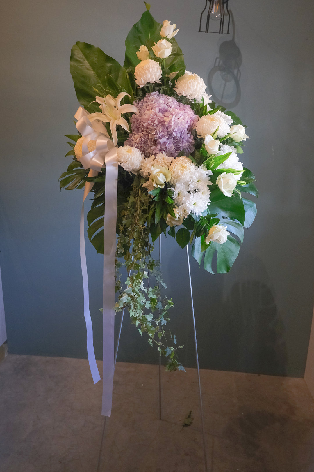 Pure, white and ethereal condolence stand featuring cream roses, white chrysanthemum and hydrangea. For same day condolences flowers delivery in Penang.  